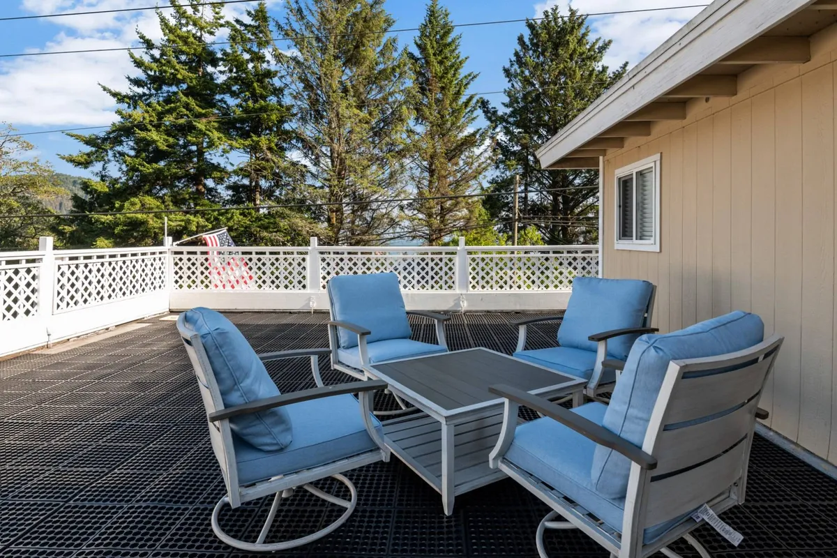 A calm exterior patio scene with comfortable seating, a table, fencing, and mature trees. The setting is peaceful and perfect for unwinding or sharing quiet moments amidst nature.