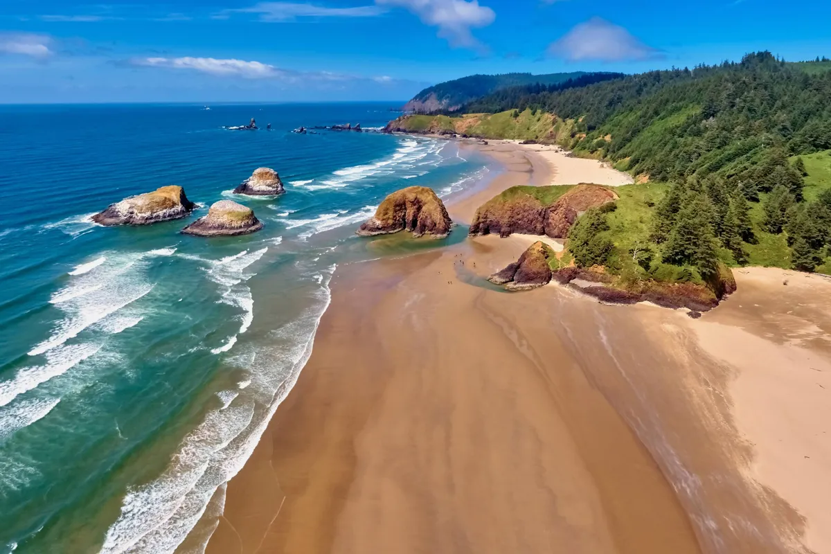 A vista of a sandy beach with rock formations, gentle waves, and green hills in the background. The beach is ideal for building sandcastles, exploring tide pools, and enjoying classic coastal activities.
