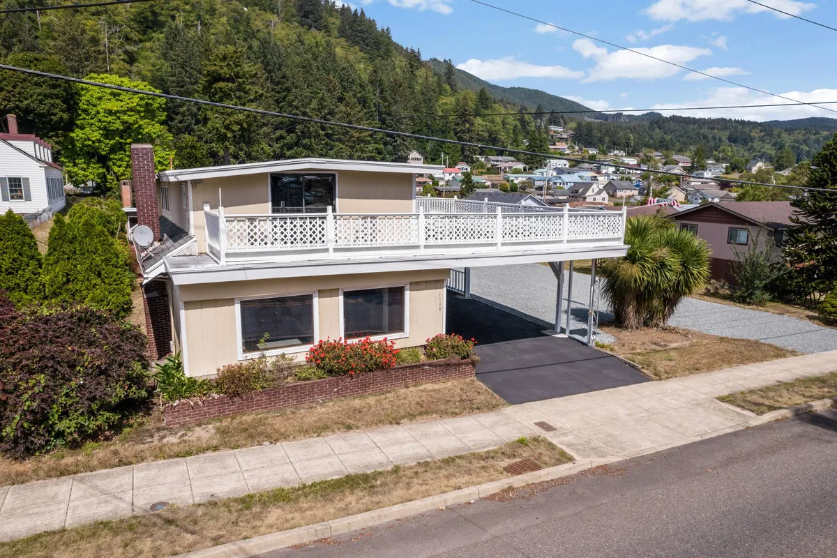 An exterior shot highlighting a large balcony overlooking a landscaped garden and driveway, surrounded by lush greenery. The inviting balcony offers an ideal spot for enjoying intimate moments while immersed in nature.