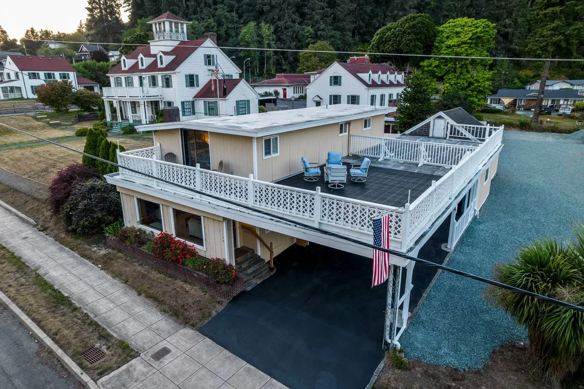 This image presents the rooftop deck where guests can enjoy sunsets, with the American flag and historic neighboring homes in the background. The atmosphere is casual and social, evoking the sense of enjoying downtime after a day of exploration on the coast.