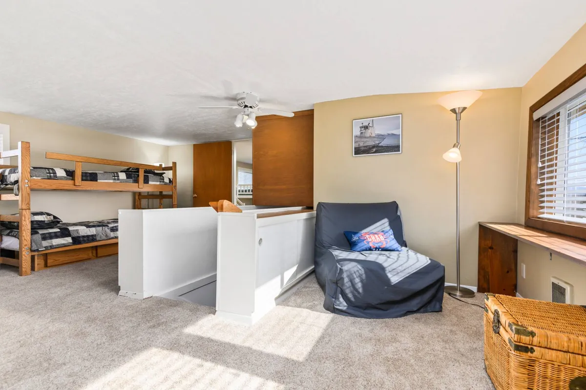 A cheerful bunk room with sturdy bunk beds, an armchair for reading or relaxing, a side table, and playful décor. The space is clearly designed for children or young travelers, offering a cozy nook for play and sleep.
